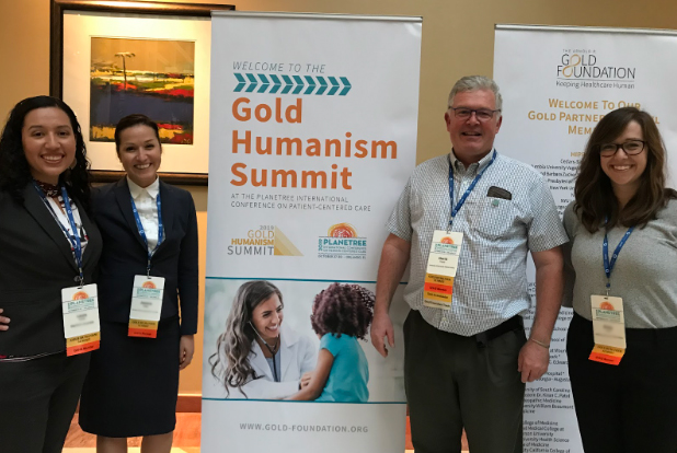 Dr. Power at a Gold Humanism Summit conference with three other colleagues standing in front of conference signs stating "Welcome to the Gold Humanism Summit".