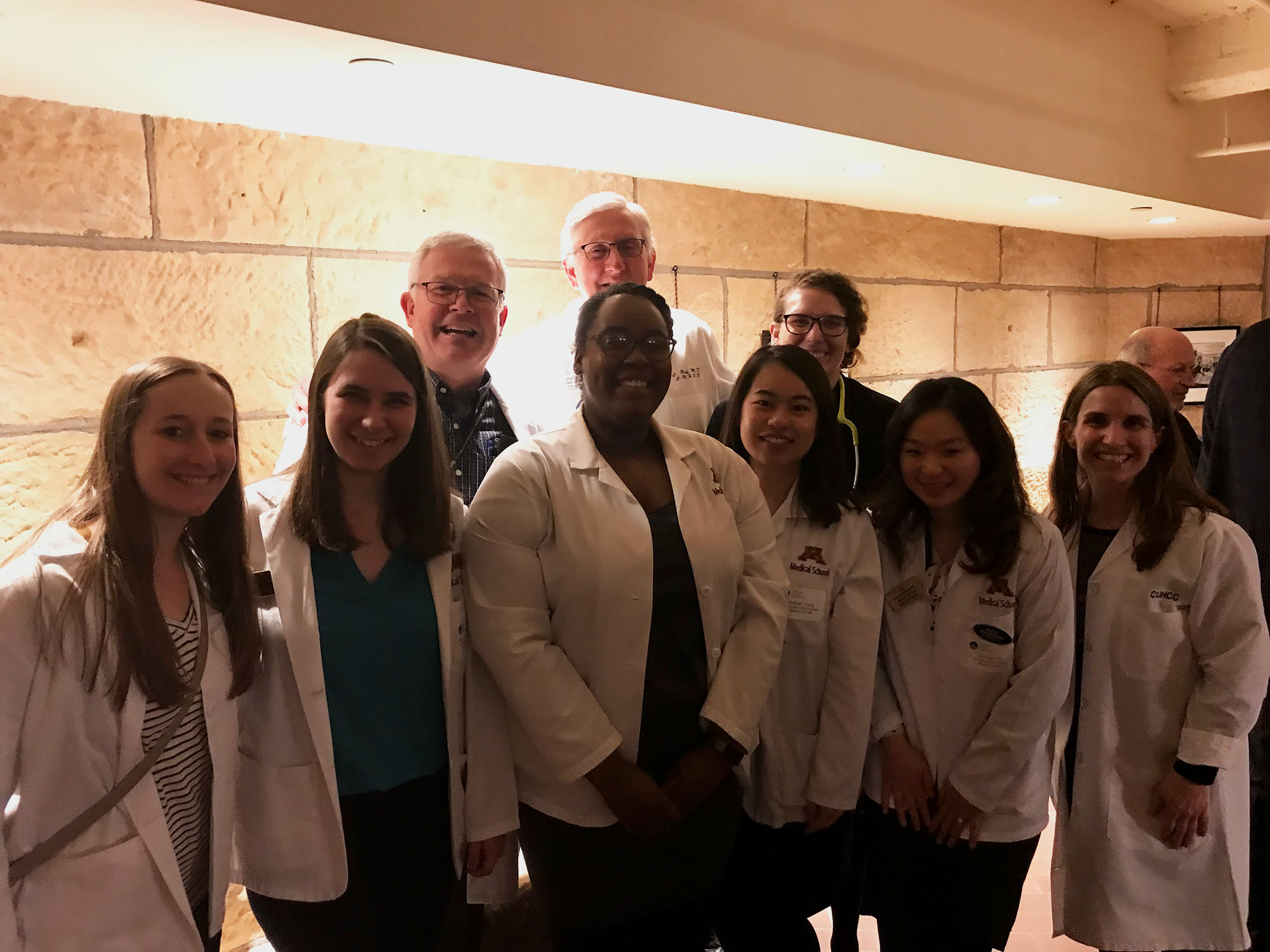 Dr. David V. Power with a group of students and colleagues standing in a small reception room.